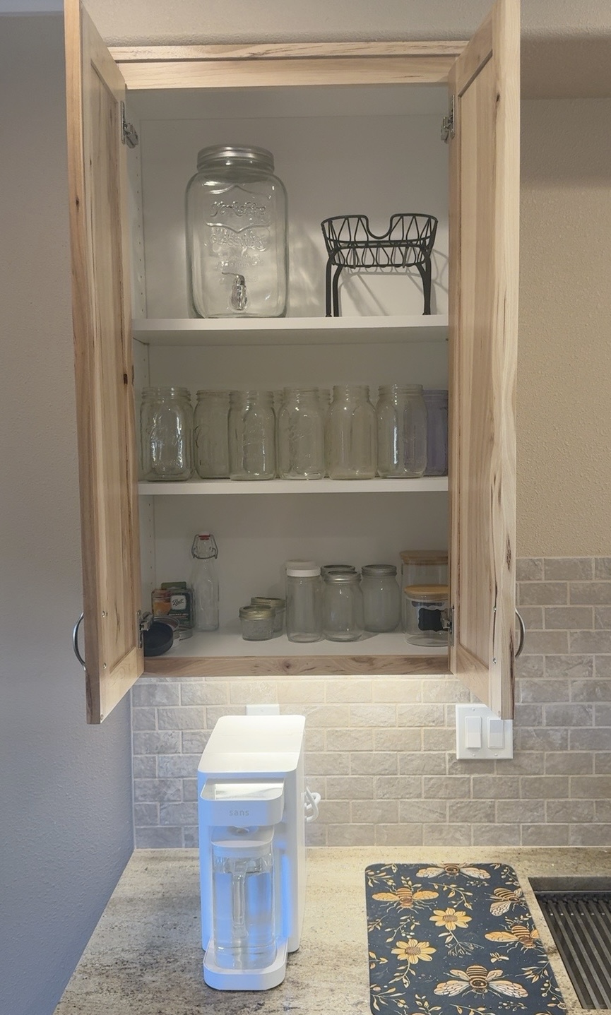 White Sans countertop water purifier beneath an open kitchen cabinet filled with Mason jars.