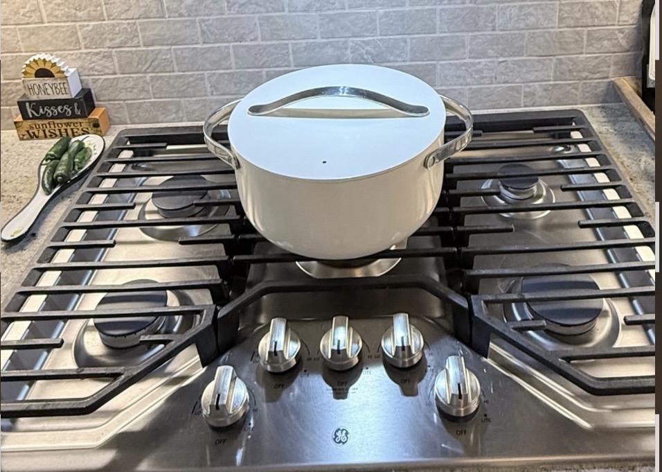 Cream-colored Caraway pot with its lid on a gas stovetop.